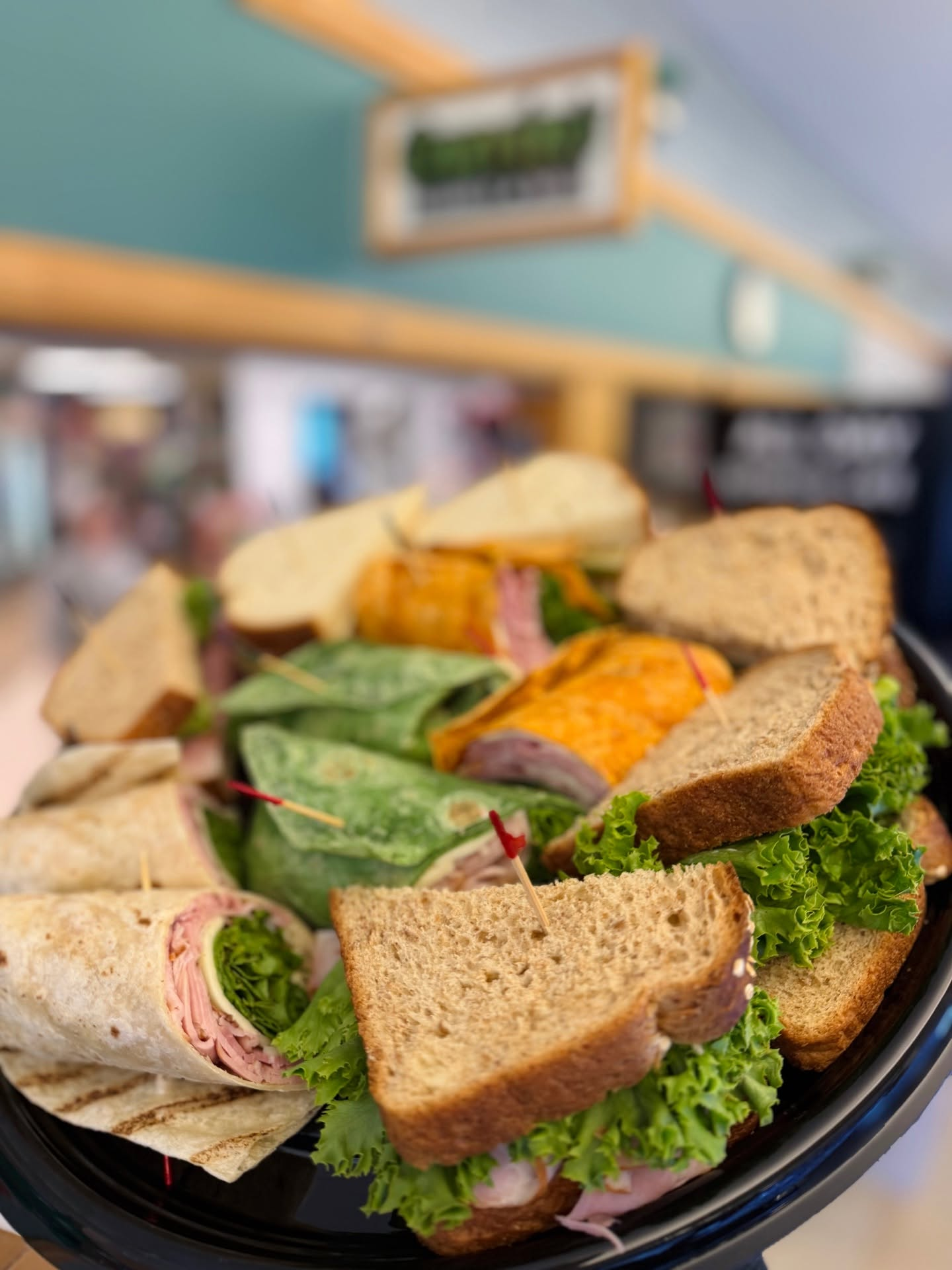 Catering at Cravin’ Market & Deli plate of sandwiches and wraps in front of a store sign